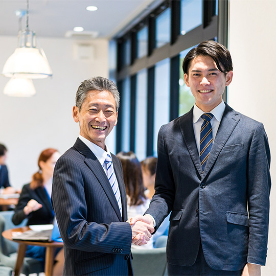 株式会社SORAQが若手と中堅社員で握手しウェブマーケティングとホームページ制作の協業を示す