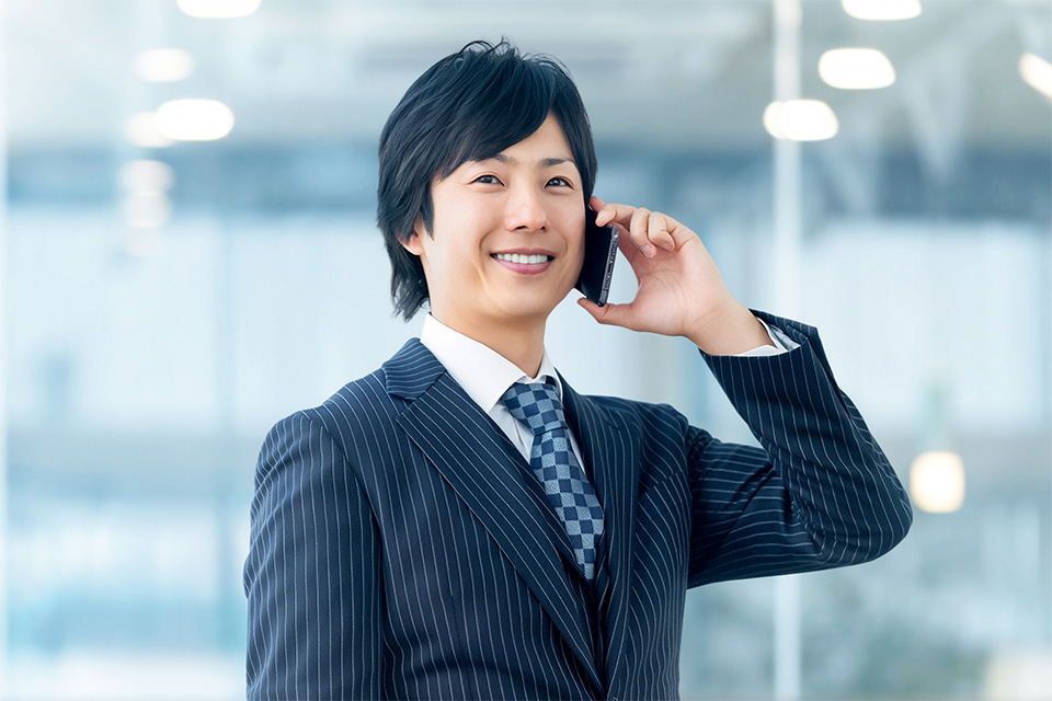 株式会社SORAQが電話で打ち合わせするスーツの男性が微笑むウェブマーケティング・ホームページ制作・運用会社の相談風景