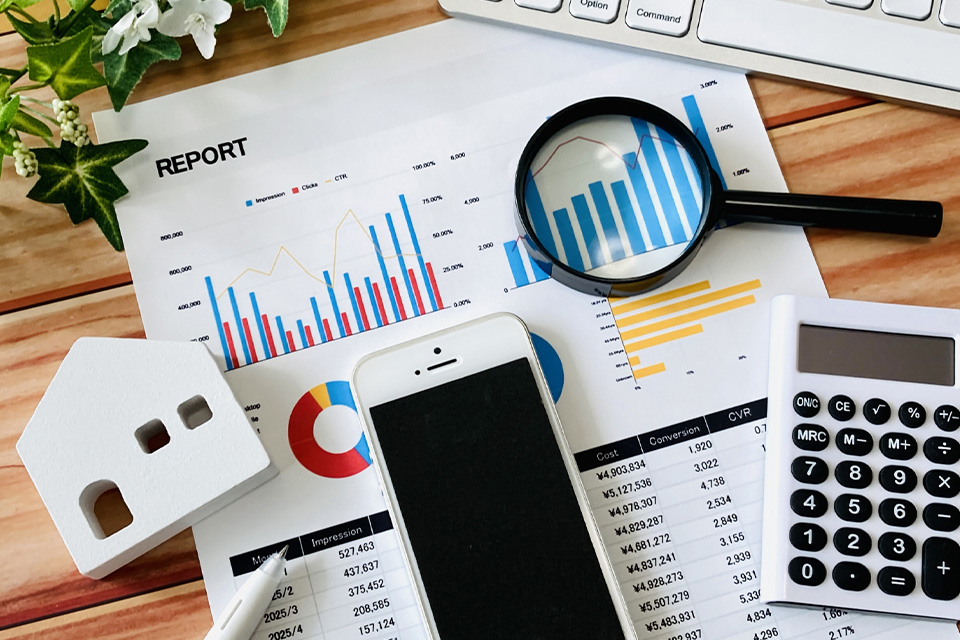 株式会社SORAQが提示したレポートと拡大鏡、スマホ、電卓でウェブマーケティング運用を検証する机上の風景
